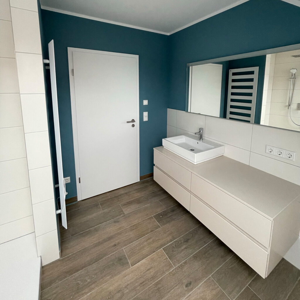 Modernes Badezimmer mit Holzfußboden; hellblaue Wände; großer Spiegel über weißem Waschbecken.