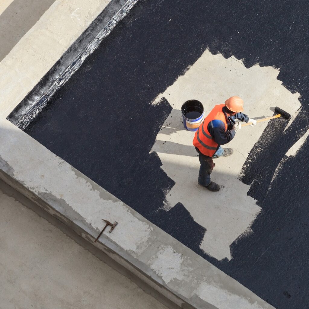 Der Arbeiter im Overall trägt eine Isolierschicht auf die Betonoberfläche auf. Blick von oben.
