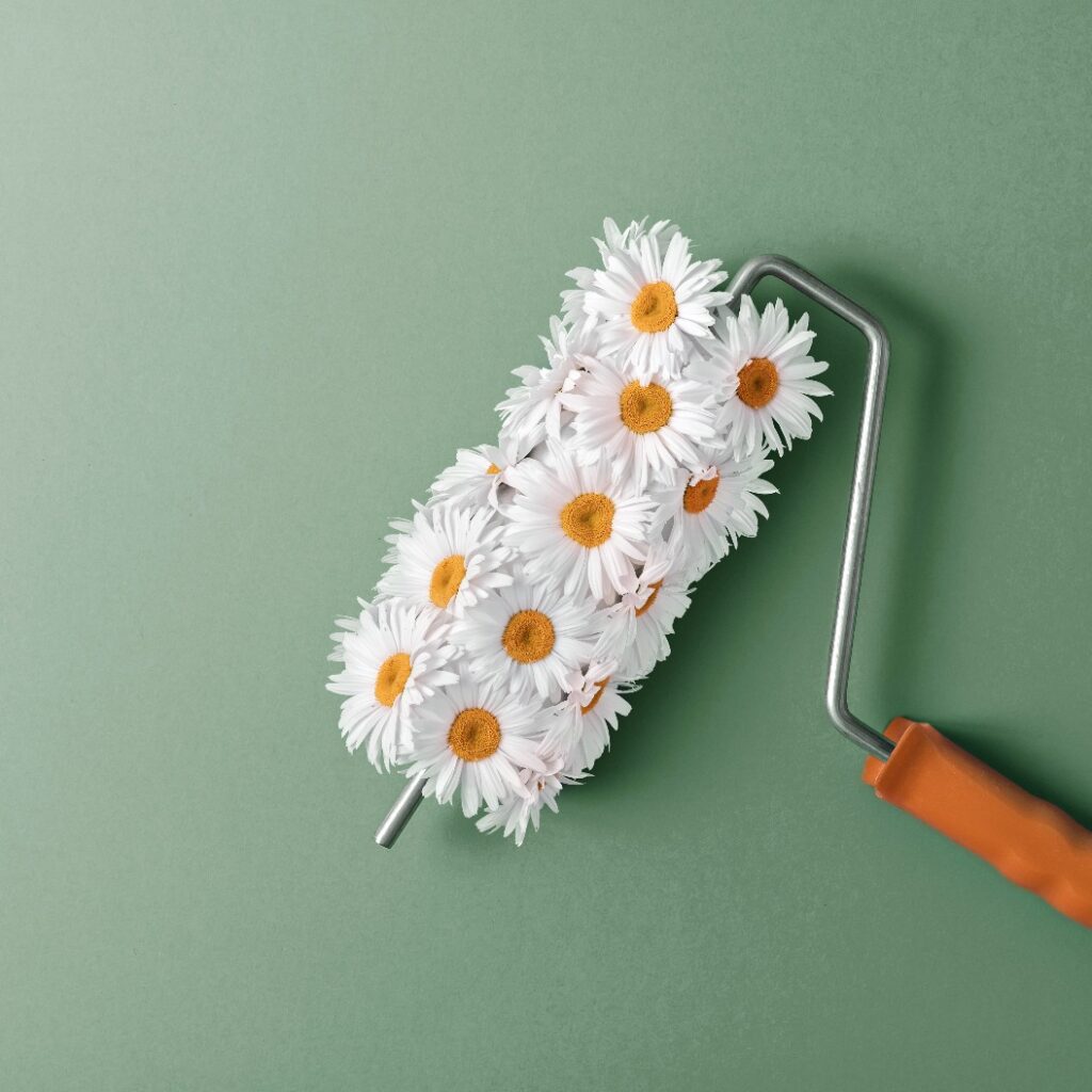 Farbroller mit weißen Gänseblümchen, die den Effekt von Blumenmalerei erzeugen, vor grünem Hintergrund. Konzept der Renovierung, Natur, Frische, Kreativität.